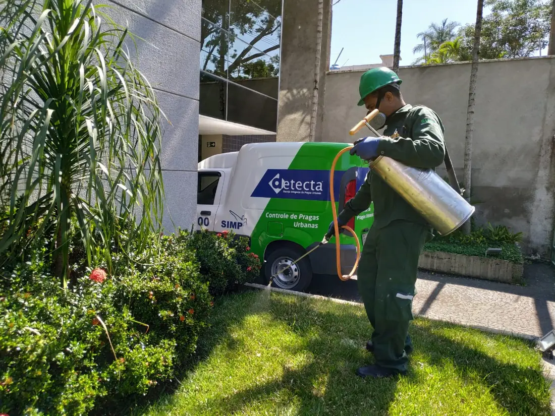 Técnico da Detecta aplicando tratamento no jardim de um prédio, com o veículo da empresa ao fundo