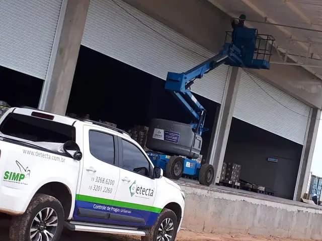 Caminhonete da Detecta e técnico em plataforma elevatória fazendo manejo de aves em galpão